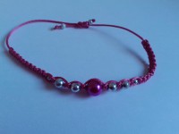pulsera de hilo rosa con perlas plateadas y rosas.